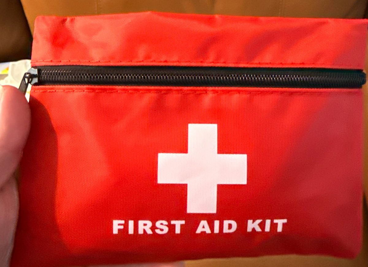 Red first aid kit with a white cross and “FIRST AID KIT” text, shown with its black zipper open.