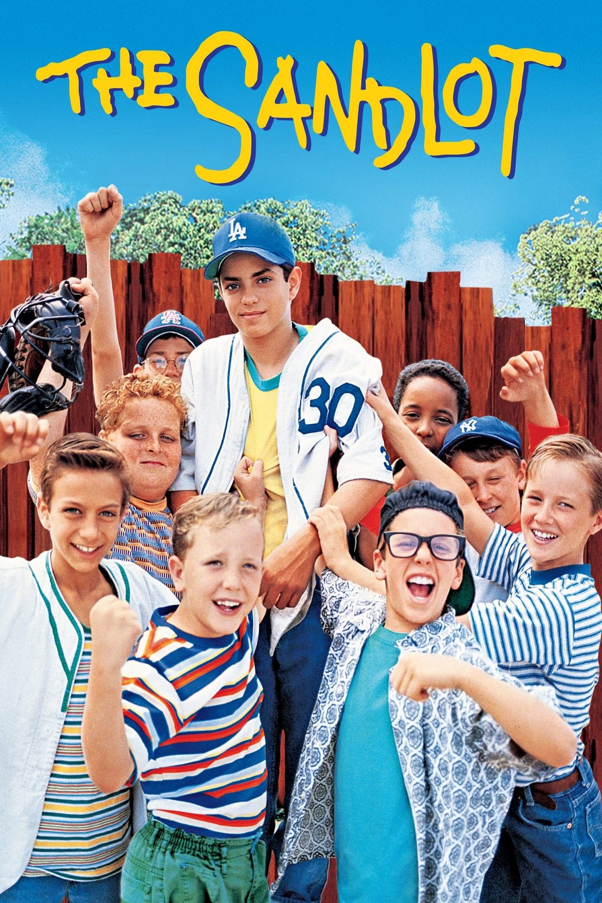 The Sandlot title above a group of boys in baseball caps cheering in front of a wooden fence.