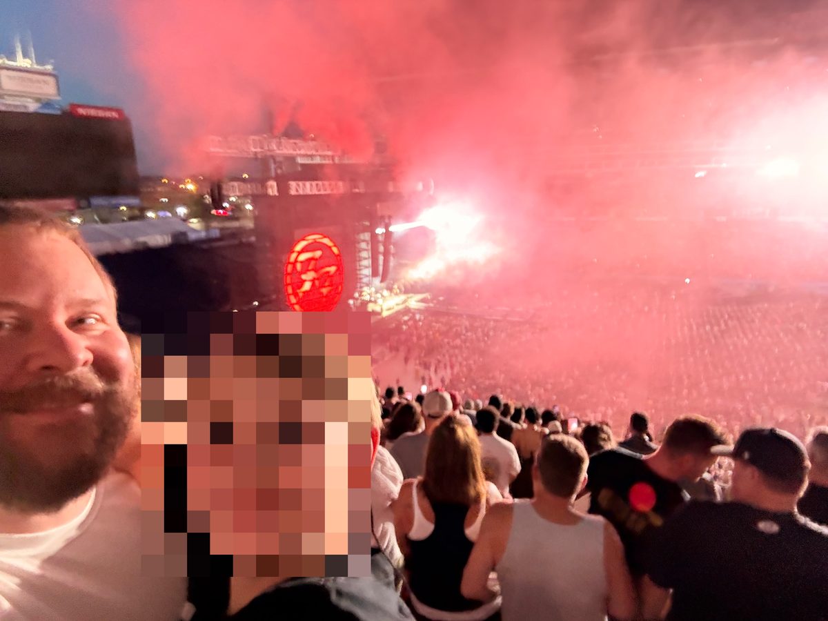 Crowd at a nighttime concert with a smiling child in the foreground and a brightly lit stage in the background.